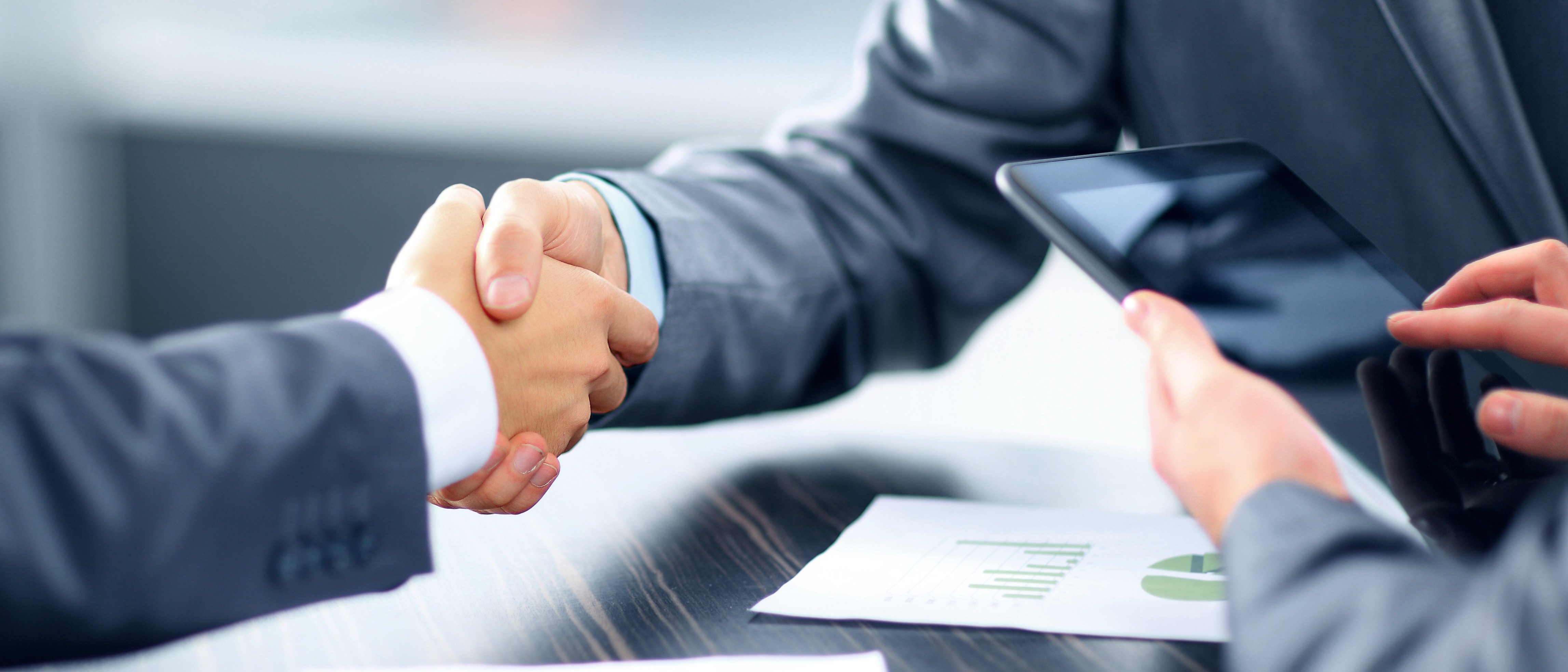 Business professionals shaking hands over a conference table, symbolizing agreement and collaboration.